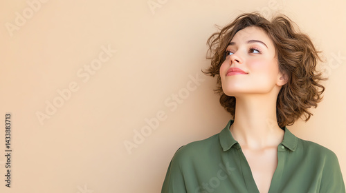 A young woman with curly hair smiles and looks thoughtfully upwards against a soft beige background, conveying a sense of serenity.