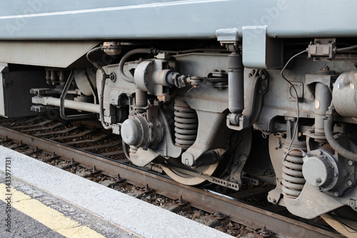 Detailed view of train undercarriage showcasing suspension system and wheel assembly at a railway station