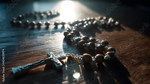 Close-up image of a wooden beaded religious necklace laying atop a wood table, with its metallic crucifix catching the light. photo