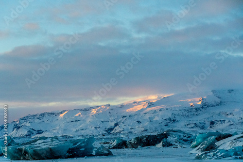 Obraz na płótnie Icebergs and huge chunks for green-blueish ice fill Jokulsarlon Glacier lagoon, as the golden hour sunlight of the early morning casts a beautiful warm glow over the glacier-filled national park in w salonie