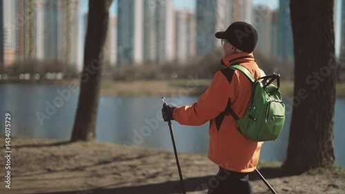 Healthy retired woman walking alone in park in sunny autumn day, urban view. Happiness and joy in old age, 60s woman practicing sport activity for save health of body and mind, nordic walking, old age
