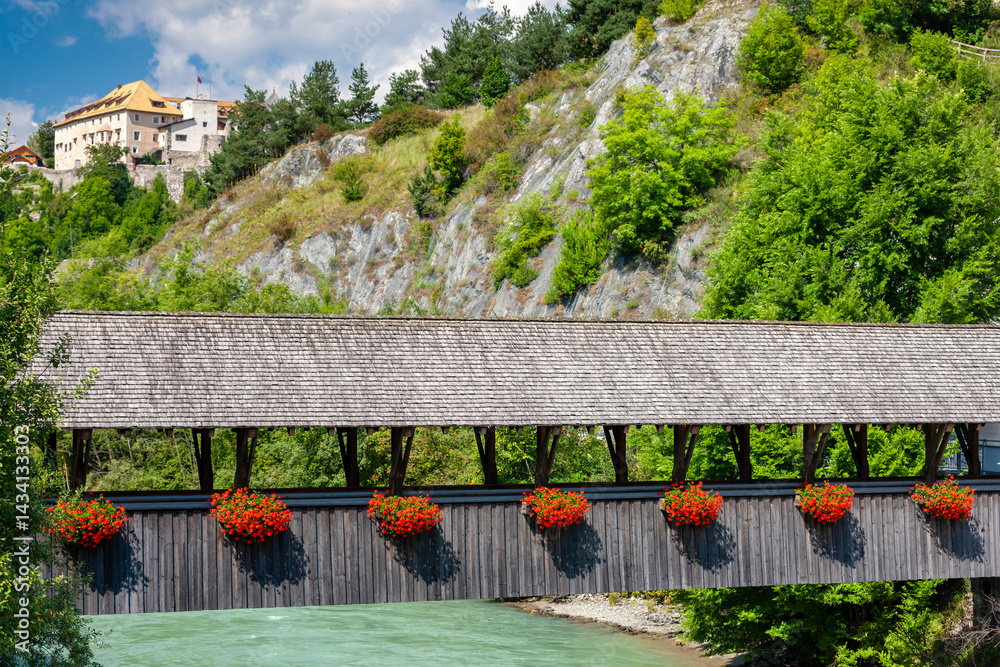 Wooden bridge with flowers crossing a river and Landeck Castle in the background