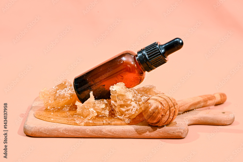 Amber glass serum dropper bottle placed on honeycomb chunks and wooden dipper on cutting board, with peach background. Natural skincare product concept featuring honey as key organic ingredient