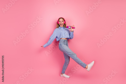 Excited young woman wearing casual outfit holding microphone during leisure time on pink background, joyful expression