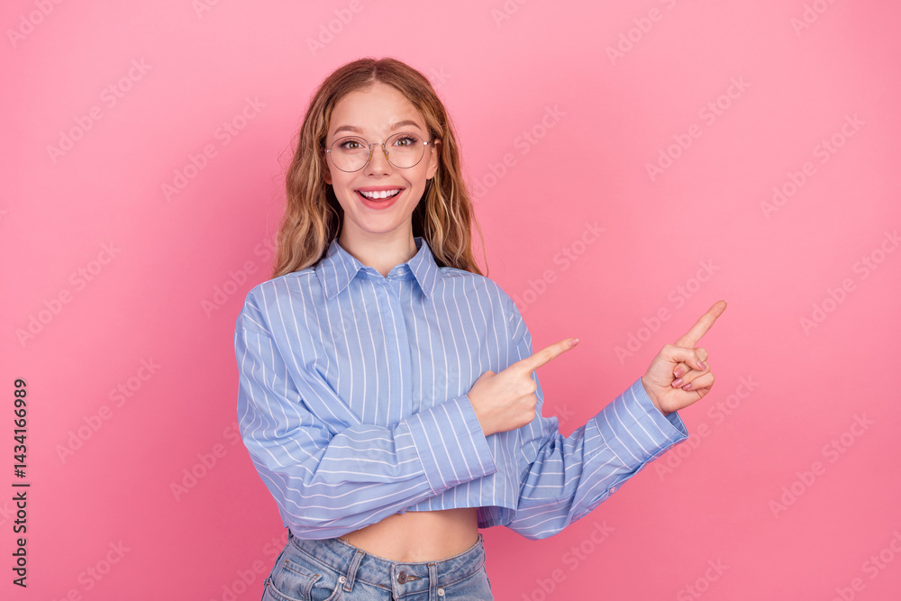 Smiling young woman in casual blue striped shirt doing pointing gestures against a pink background, expressing happiness and positivity Smiling young woman in casual blue striped shirt doing pointing gestures against a pink background, expressing happiness and positivity