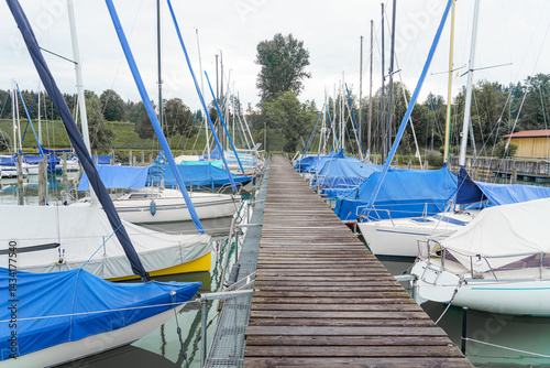 Sailing boats lined up at a serene marina in an overcast sky during early morning hours
