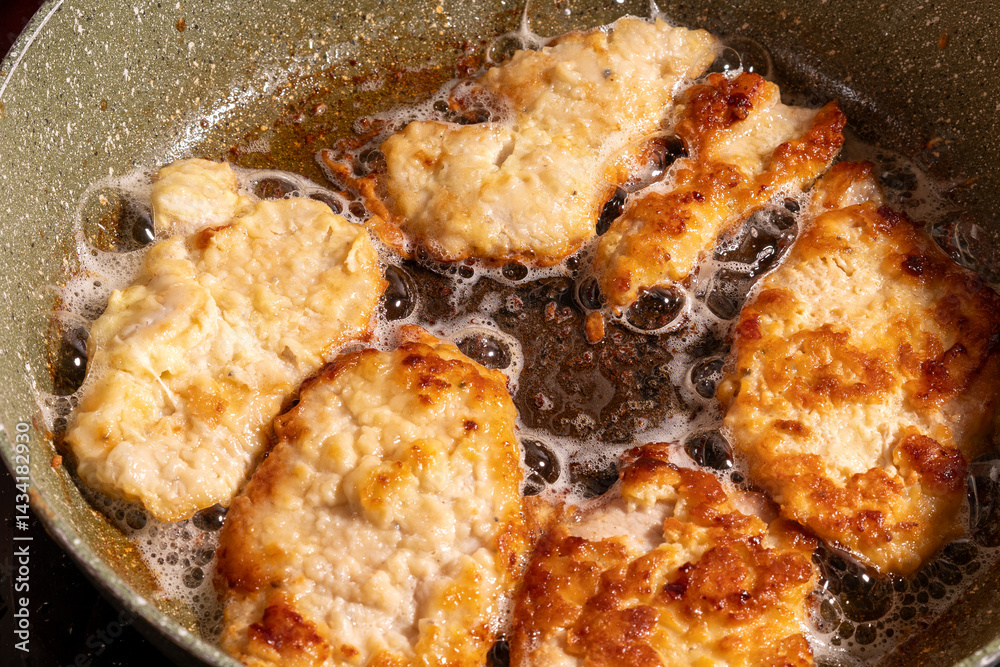 Golden brown breaded chicken pieces sizzle in a pan of hot oil, with bubbles forming around them.