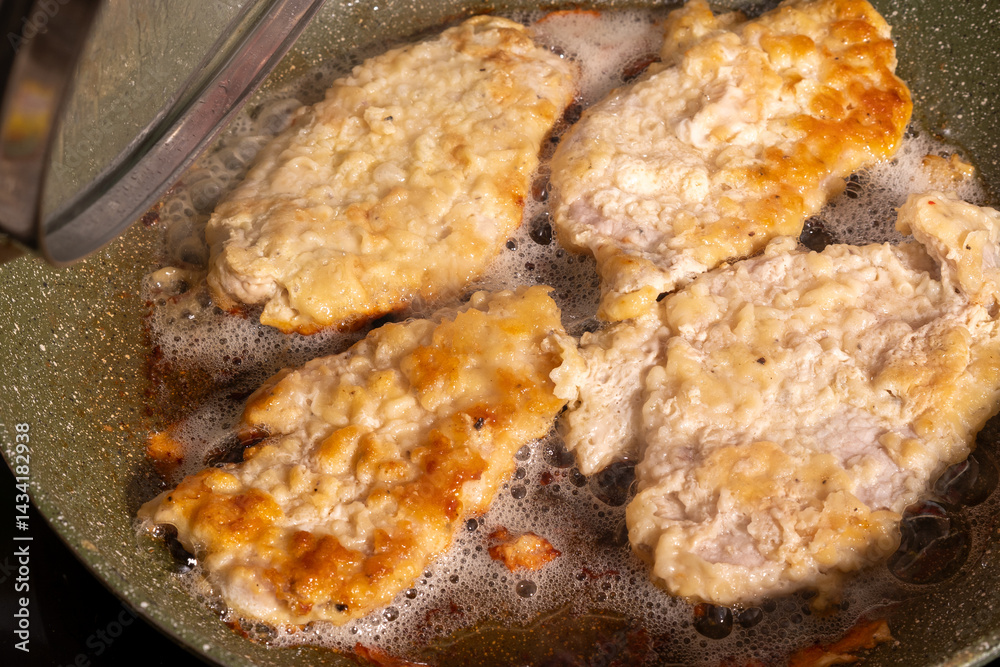 Four golden-brown breaded chicken pieces sizzling in bubbling oil inside a pan with a speckled surface.