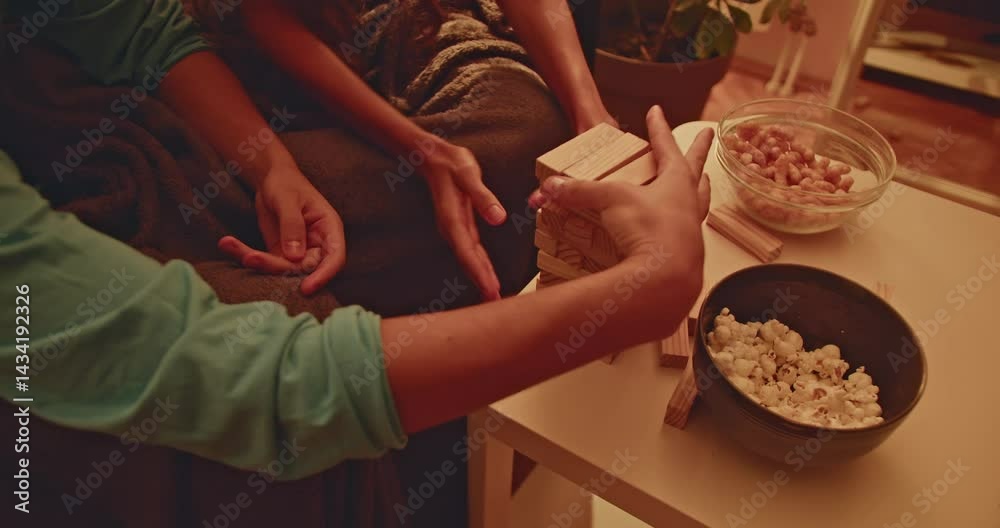 Couple playing Jenga. A young couple plays a game at home in the evening. They have snacks and drinks.