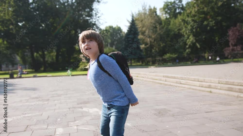 Funny little Slavic guy wearing blue clothes flying kite near monument. Portrait of playful Caucasian child with backpack. Outdoors. Autumn. Funny little Slavic guy wearing blue clothes flying kite near monument. Portrait of playful Caucasian child with backpack. Outdoors. Autumn.