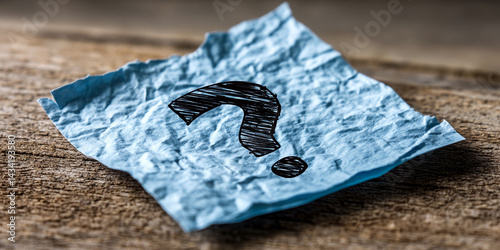 Blue crumpled paper with a hand-drawn question mark rests on wood, symbolizing uncertainty, inquiry, or the need for answers