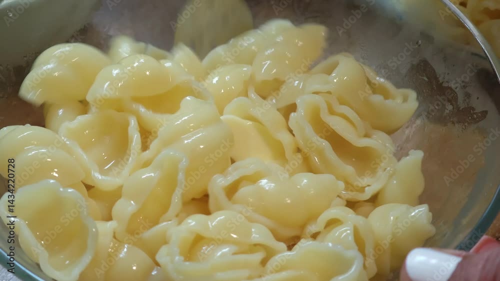 Butter is being mixed into freshly cooked pasta shells with a fork in a glass bowl Butter is being mixed into freshly cooked pasta shells with a fork in a glass bowl
