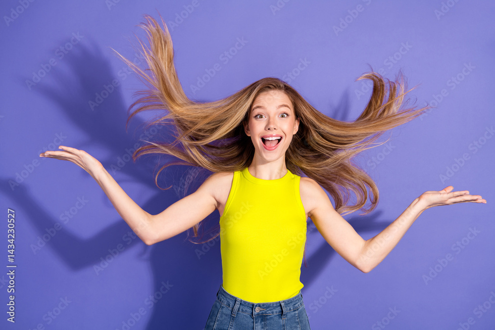 Excited young woman with flowing hair wearing a yellow top posing joyfully against a vibrant purple background