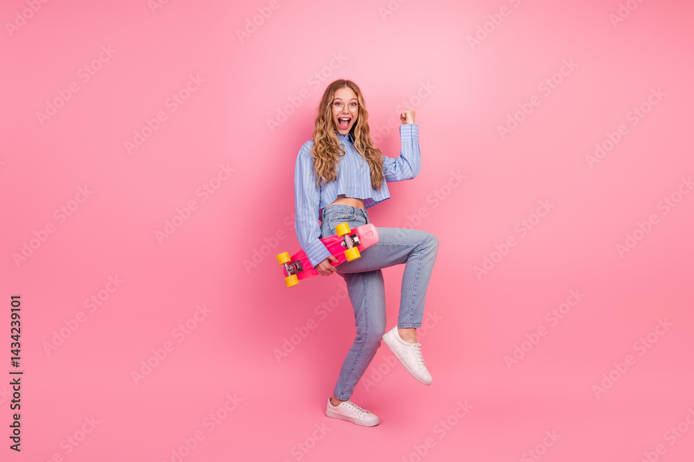 Cheerful female holding vibrant skateboard against pink backdrop, expressing youthfulness and trendy lifestyle