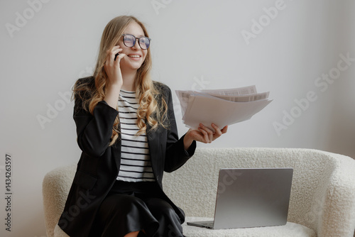 Businesswoman engaged in a phone call while holding documents in a modern office setting