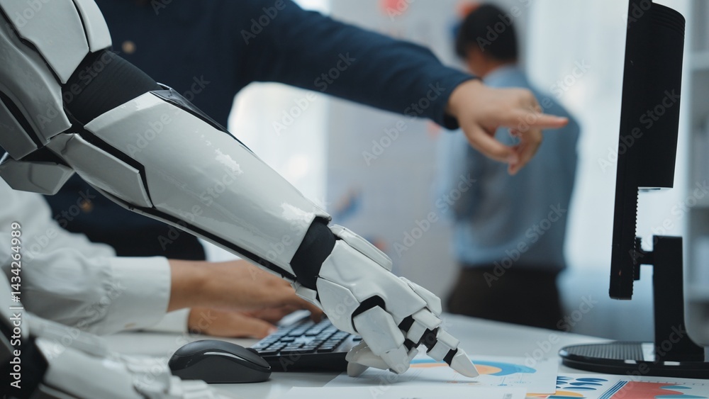 A robotic arm interacts with a computer in a modern office setting, symbolizing the integration of technology and human effort in the workplace.Noogenesis A robotic arm interacts with a computer in a modern office setting, symbolizing the integration of technology and human effort in the workplace.Noogenesis