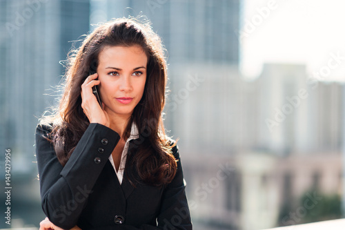 Pretty young businesswoman talking on mobile phone with downtown buildings skyline in background