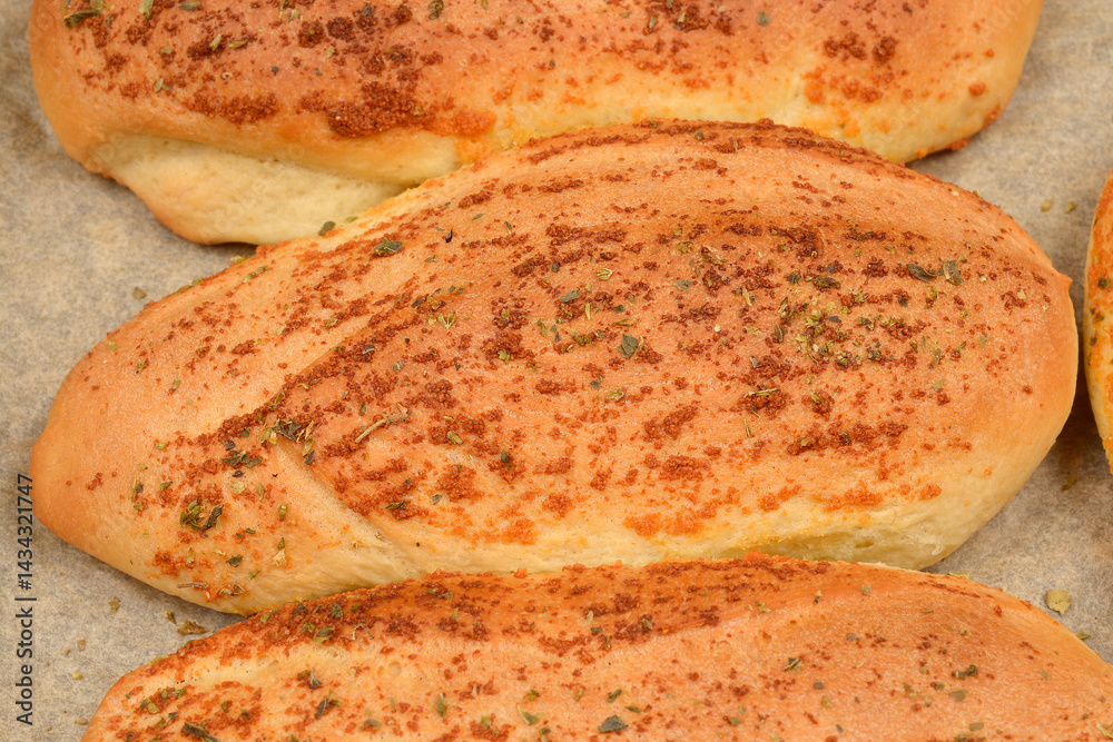 Several golden-brown garlic and oregano rolls are arranged on a baking pan lined with parchment paper
