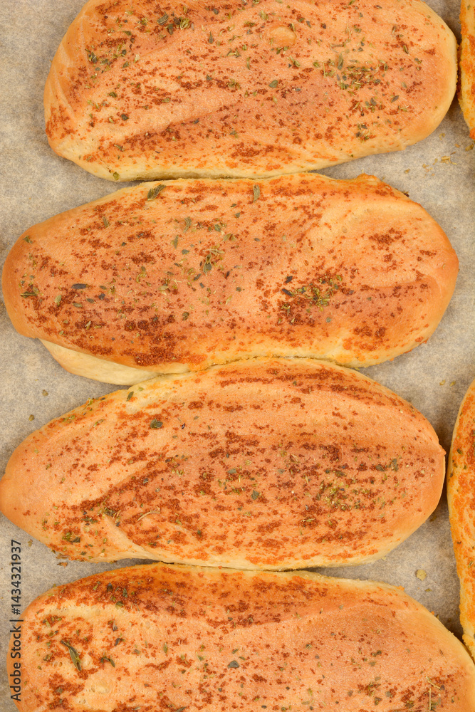 Several golden-brown garlic and oregano rolls are arranged on a baking pan lined with parchment paper