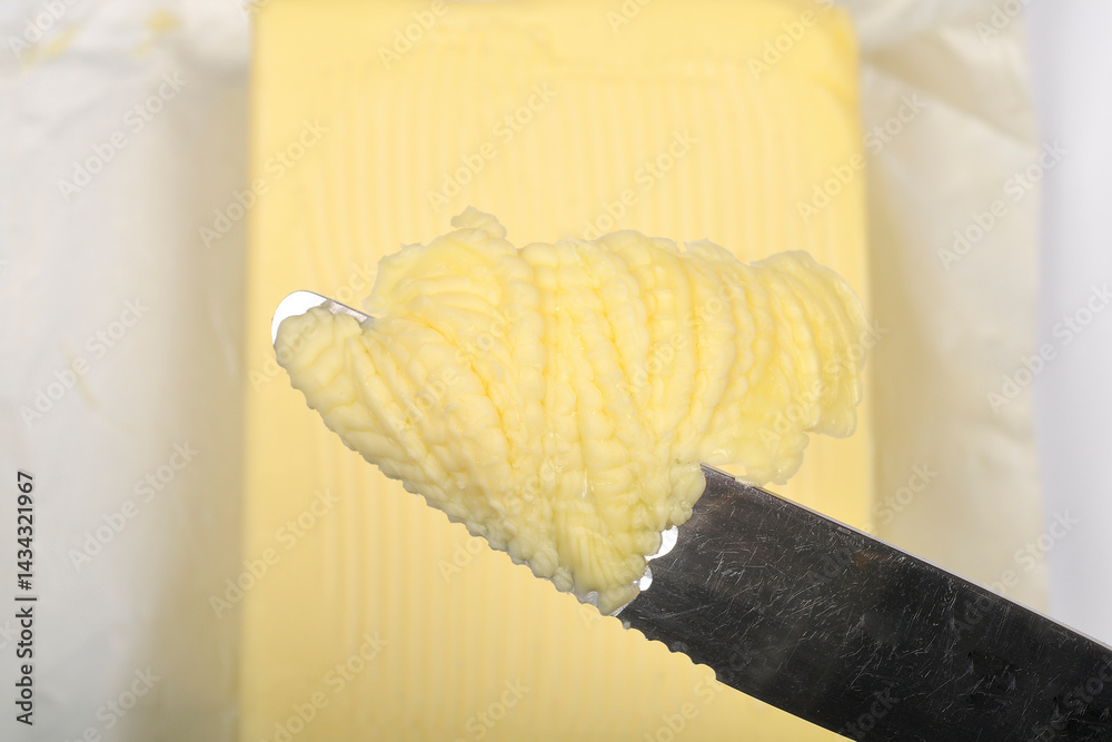 A close-up shot shows a curl of yellow butter on a knife blade against a blurred background of a butter block and white paper