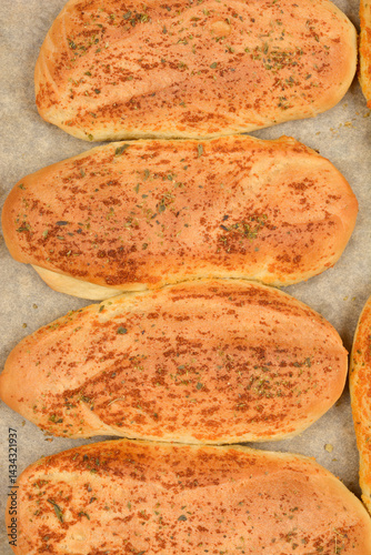 Several golden-brown garlic and oregano rolls are arranged on a baking pan lined with parchment paper