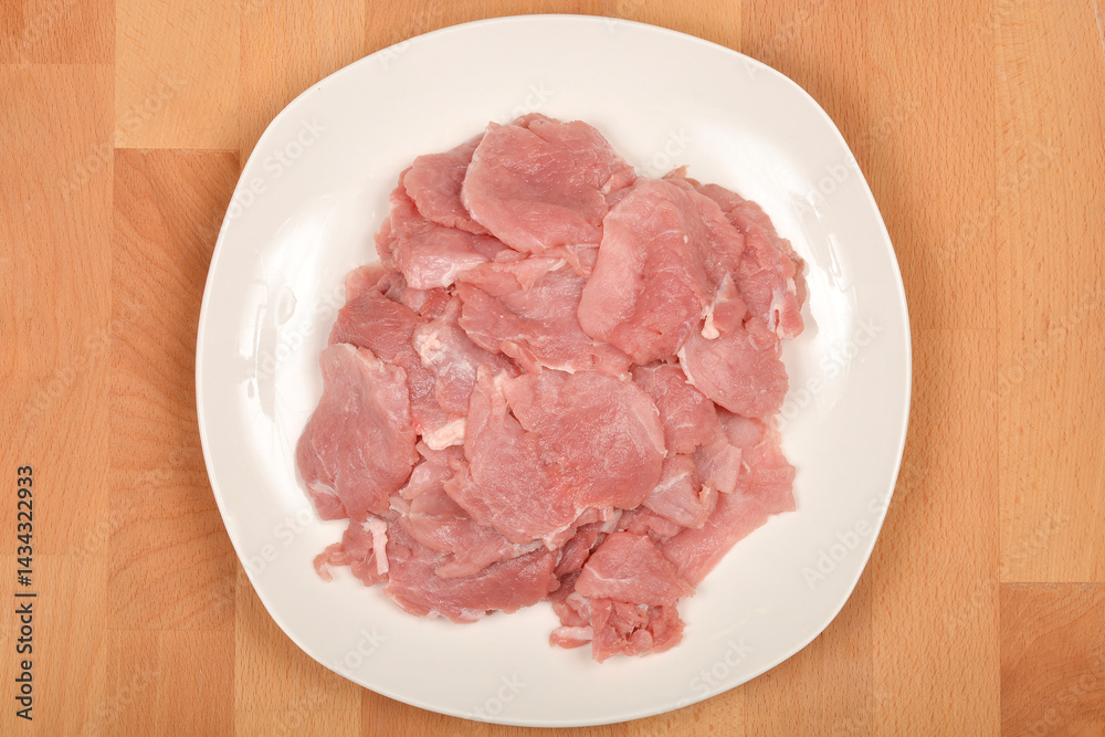 Thinly sliced raw pork tenderloin is arranged on a white plate set on a wooden surface, captured from a top-down perspective