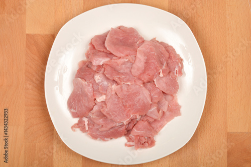 Obraz na płótnie Thinly sliced raw pork tenderloin is arranged on a white plate set on a wooden surface, captured from a top-down perspective w salonie