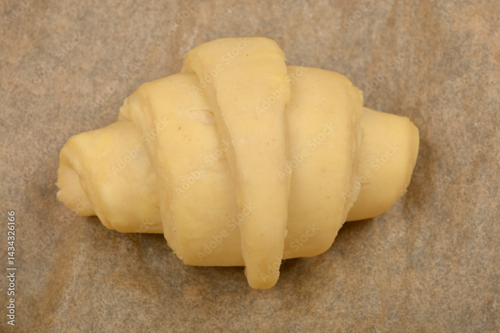 A single, unbaked croissant dough rests on a piece of parchment paper, ready for the oven