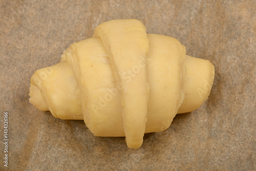 Obraz na płótnie A single, unbaked croissant dough rests on a piece of parchment paper, ready for the oven w salonie