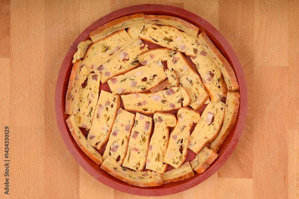A top-down view shows slices of prisnac, a savory egg, bacon and cheese pie, arranged in a round silicone mold on a light brown wooden surface