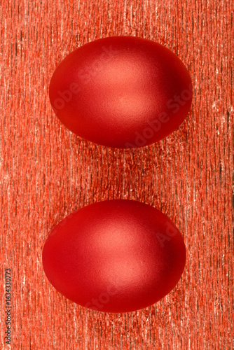 Obraz na płótnie Two metallic red eggs are positioned side-by-side on a textured, shimmering red surface w salonie