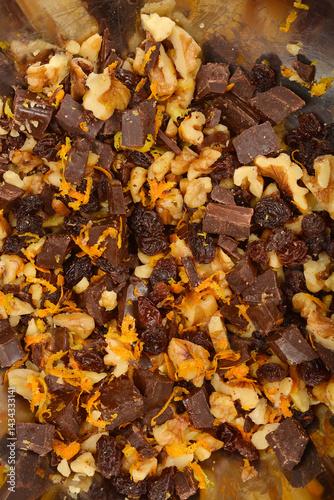 Obraz na płótnie A tightly cropped top-down view shows a mixture of walnuts, dark chocolate chunks, raisins, and vibrant orange zest, possibly with some lemon zest, in a metal bowl w salonie