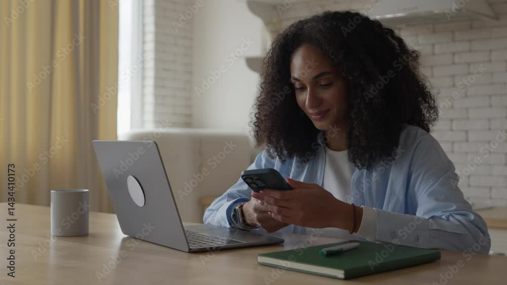 Woman Smiling At Phone Screen While Working On Laptop At Cozy Kitchen Table Woman Smiling At Phone Screen While Working On Laptop At Cozy Kitchen Table
