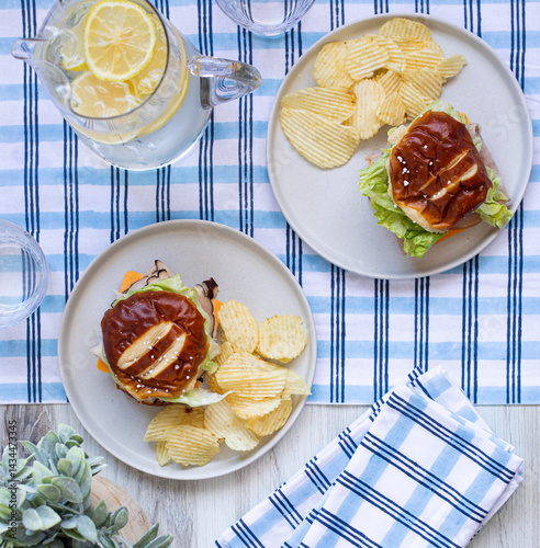 Table top picnic lunch with plaid tablecloth and sandwiches on plates with a pitcher of water with lemons