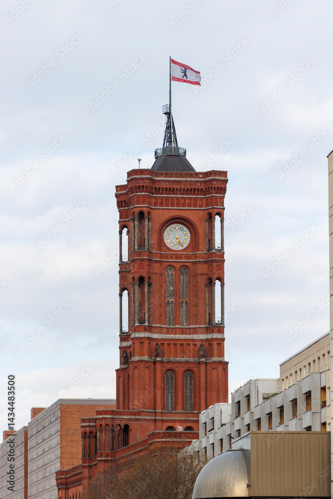 Obraz premium Historical red clock tower in Berlin, Germany, showcasing its intricate architecture and a flag waving atop. Ideal for themes of history and city landmarks.