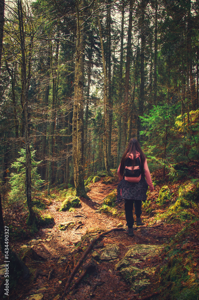 Fototapeta premium Teenage girl walking alone on a beautiful forest trail in autumn, enjoying the peaceful atmosphere and colorful fallen leaves all around.