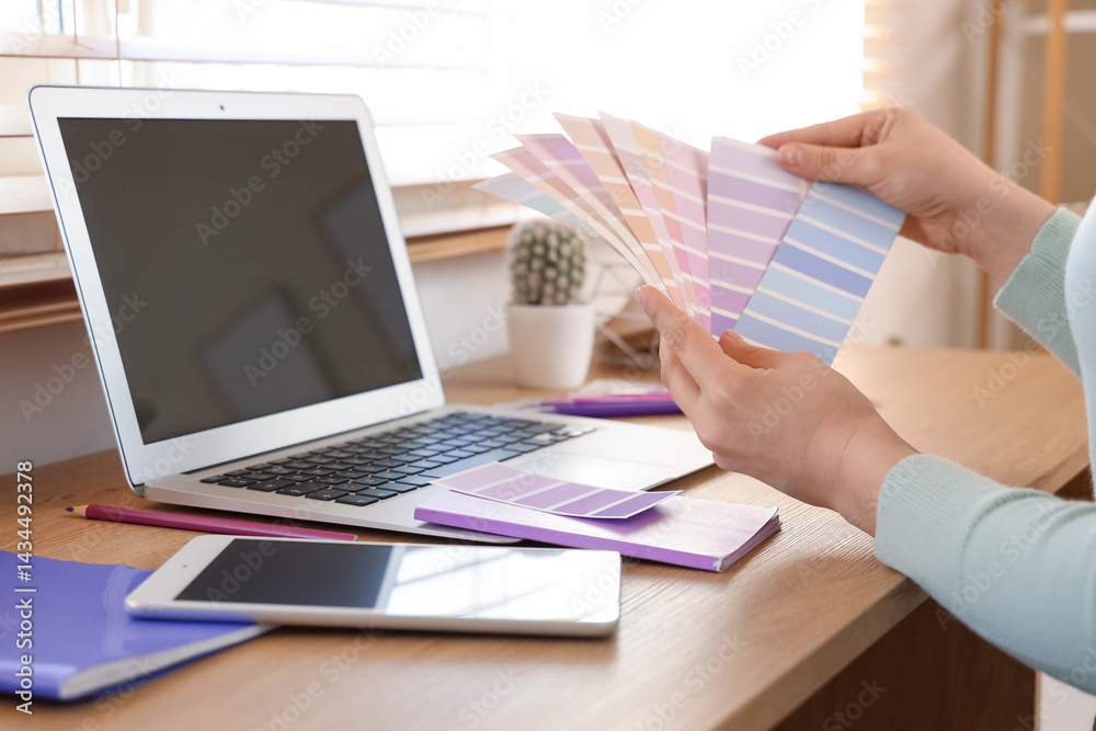 Young woman with laptop, tablet computer and paint palette swatches choosing lilac color near table at home, closeup