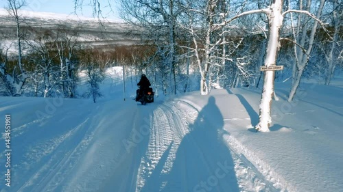 Snowmobiling tourists gliding through pristine white forest landscape, experiencing winter adventure in scenic Finnish Lapland wilderness under bright sunlight
