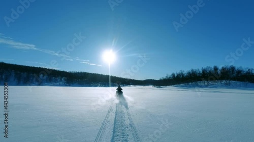 Powerful snowmobile racing across snow covered frozen lake under bright winter sunlight, carving trail against pristine arctic landscape in Lapland wilderness