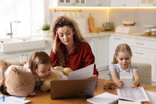 Work-family balance. Single mother with document and her daughters at table in kitchen