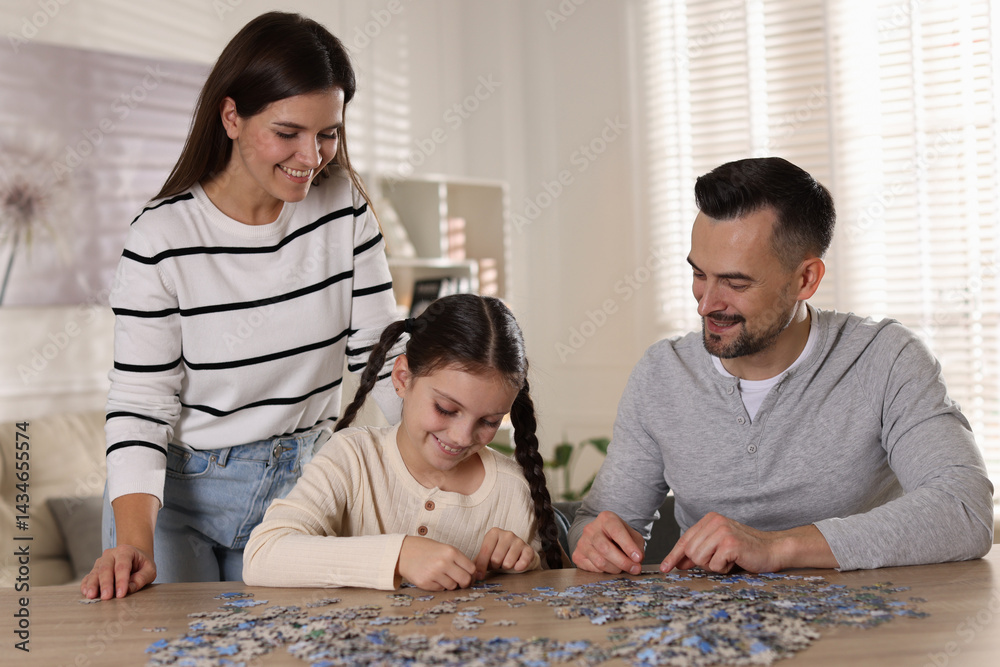 Fototapeta premium Happy parents and their daughter solving puzzle together at wooden table indoors