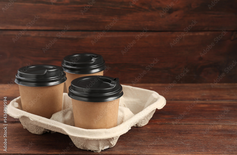 Paper coffee cups in cardboard holder on wooden table. Space for text