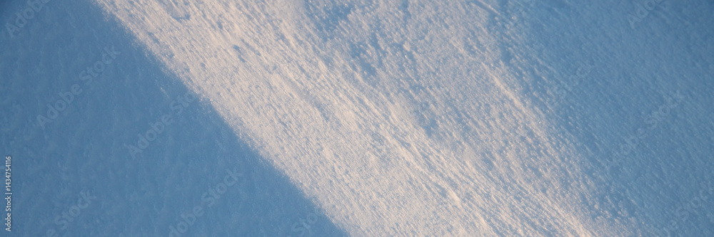 Beautiful winter background with snowy ground. Natural snow texture. Wind sculpted patterns on snow surface. Wide panoramic texture for background and design. Closeup top view with copy space.