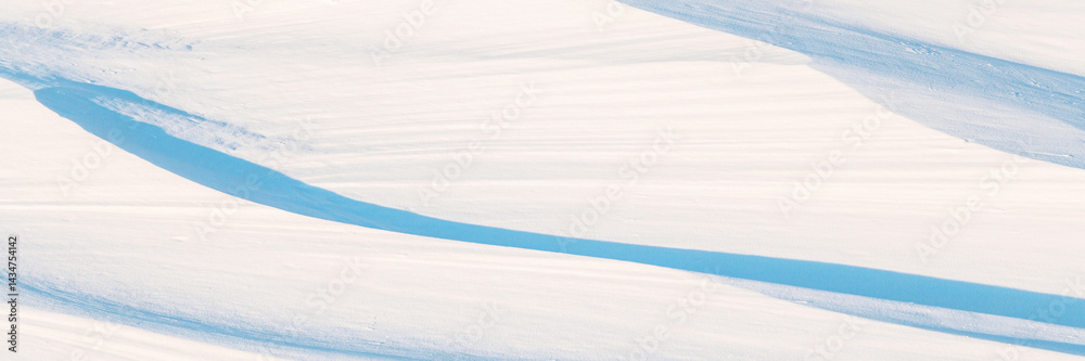 Wide panoramic winter background with snowy ground. Natural snow texture. Wind sculpted patterns on snow surface.