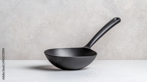 A black ladle resting on a white surface, against a neutral background.