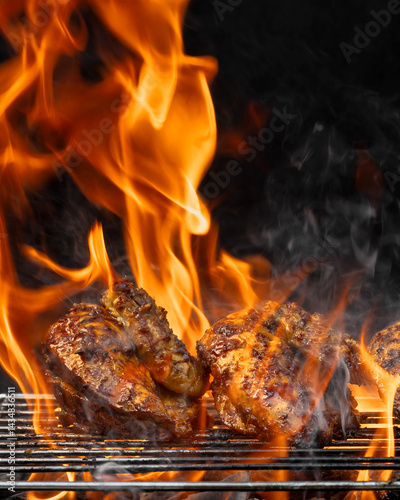 Two pieces of chicken are cooking on a grill, with flames