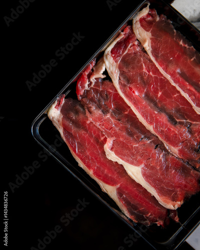 A slab of meat is displayed in a black tray