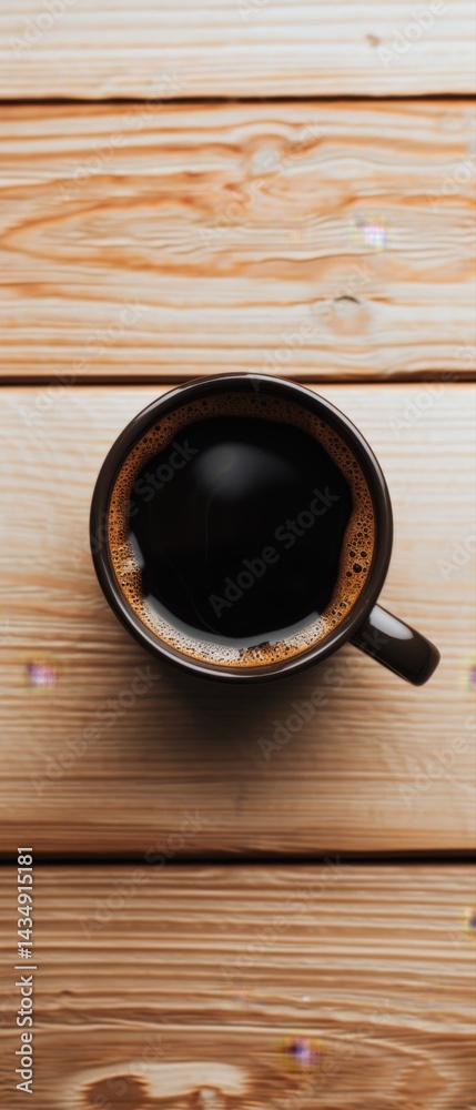 Fototapeta premium A top-down view of a black coffee cup resting on a wooden surface, highlighting a warm, cozy atmosphere.