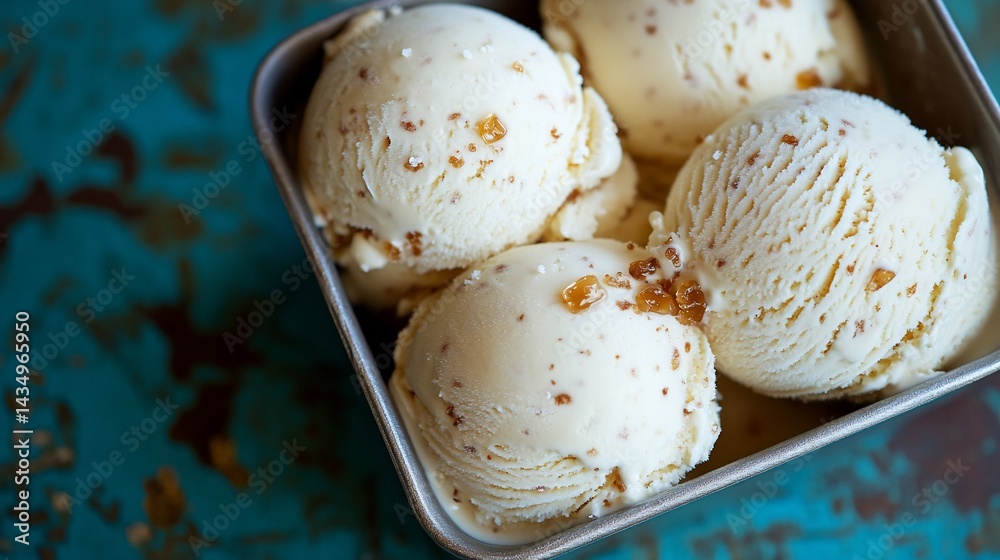 Creamy, light-yellow ice cream scoops in a small metal tin, topped with crunchy bits