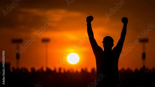 Silhouette of a man raising his arms in celebration against a vibrant orange sunset with stadium lights in the background.